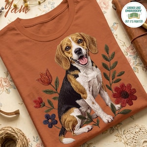 Puede incluir: Una camiseta de color óxido con un gráfico de un perro beagle sentado entre varias flores. El perro tiene pelaje marrón, negro y blanco con la boca abierta. El diseño floral incluye flores rojas y azules con hojas y tallos verdes.