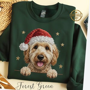 Peut inclure: Sweat-shirt vert forêt avec un chien souriant portant un bonnet de Père Noël. Le chien a des poils brun clair et des étoiles dorées. Le texte "Customize Me!" est dans un cercle doré. Les mots "Forest Green" sont écrits en cursive en bas.