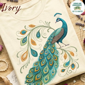 May include: An ivory t-shirt featuring a detailed peacock graphic with blue, green, and gold feathers. The design includes text that reads Ivory and a circular badge stating Looks Like Embroidery But It's Printed.