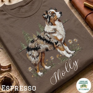 May include: A brown t-shirt featuring a graphic of an Australian Shepherd dog with paisley and floral patterns on its fur. The dog is surrounded by pine trees and daisies. The name Molly is written in white script below the dog illustration.