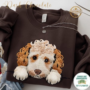 Può includere: Una felpa girocollo color marrone cioccolato scuro con una stampa dettagliata in stile ricamo raffigurante un cane dal pelo riccio bianco e marrone dorato. Il testo "Dark Chocolate" appare in alto, con i badge "CUSTOMIZE ME!" e "LOOKS LIKE EMBROIDERY BUT IT'S PRINTED!".