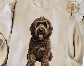 May include: A beige crew neck sweatshirt with a detailed illustration of a brown Goldendoodle dog. The dog is centered on the front of the sweatshirt. A gold sticker with the words "Customize Me!" is visible.