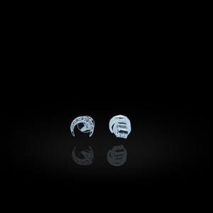 以下が含まれることがあります： 黒い背景に2つの銀色のイヤリング。1つのイヤリングは、小さな透明な石が付いた三日月型です。もう1つのイヤリングは、様式化された抽象的なデザインです。両方のイヤリングが下に反射しています。