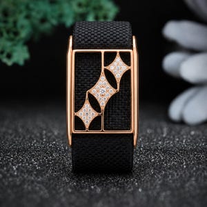 May include: A black fabric watch band featuring a rectangular rose gold metal frame. The frame contains three interconnected diamond-shaped cutouts, each encrusted with small, clear, sparkling stones arranged in a geometric pattern.