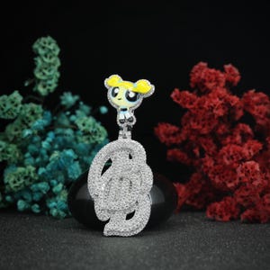 Op de afbeelding: Een zilveren ketting met een bedel in de vorm van een cartoonfiguur. De bedel toont een meisje met geel haar in een blauwe jurk op een witte achtergrond. De bedel is bedekt met heldere zirkonia-stenen.