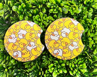 May include: Two yellow and white rubber ducky coasters with a repeating pattern of rubber duckies. The coasters are on a green background.