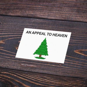 May include: A rectangular white card featuring a green pine tree illustration with a brown trunk and the black text AN APPEAL TO HEAVEN printed in a bold sans-serif font across the top portion of the card surface.