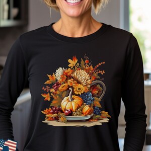 May include: A black long-sleeved shirt with a colorful autumn harvest design. The design features a cornucopia overflowing with pumpkins, grapes, and fall foliage.