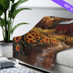 May include: A throw blanket featuring a painting of a red barn with a field of sunflowers in the foreground. The blanket is 60 inches by 80 inches.