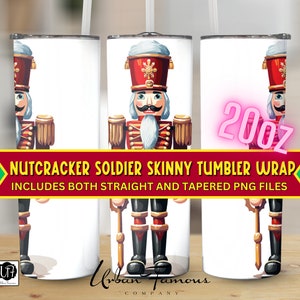 Op de afbeelding: Een digitaal ontwerp voor een skinny tumbler wrap met een Notenkraker-soldaat in een rood-gouden uniform. Het ontwerp bevat zowel rechte als taps toelopende PNG-bestanden. De tekst "NUTCRACKER SOLDIER SKINNY TUMBLER WRAP INCLUDES BOTH STRAIGHT AND TAPERED PNG FILES" is in de afbeelding opgenomen.