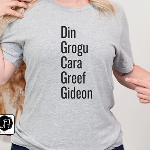 May include: Gray t-shirt with the names Din, Grogu, Cara, Greef, and Gideon printed on it in black.