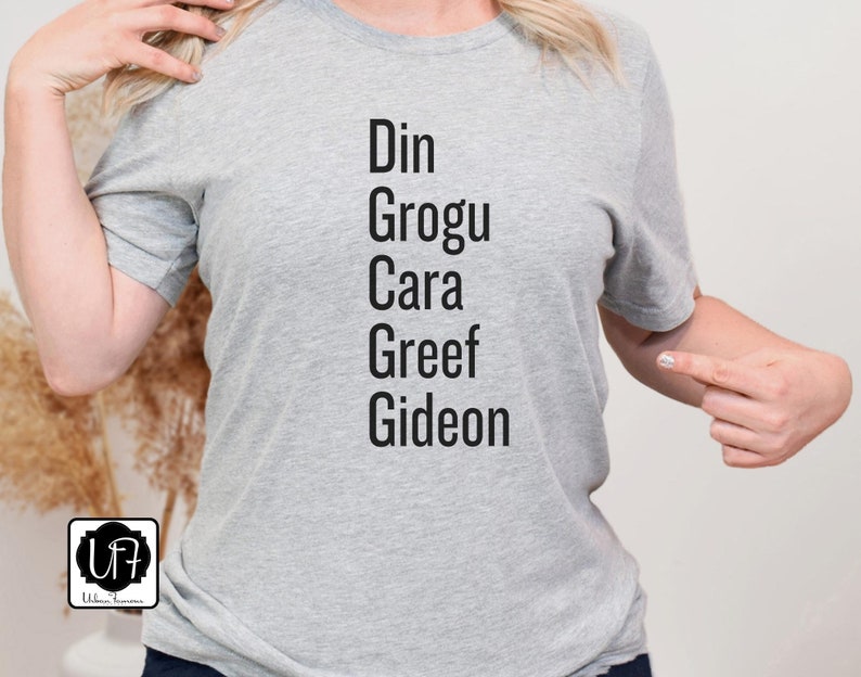 May include: Gray t-shirt with the names Din, Grogu, Cara, Greef, and Gideon printed on it in black.