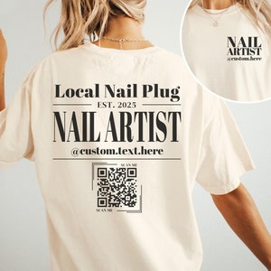 May include: A white t-shirt with a black design that says "Local Nail Plug Est. 2025 Nail Artist @custom.text.here" and a QR code that says "Scan Me". The shirt is on a model and the background is white.