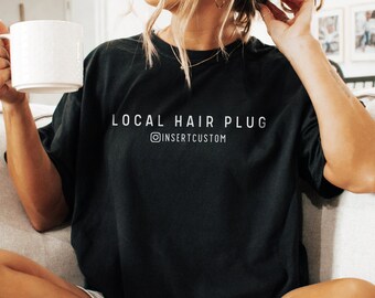 Pode incluir: Camiseta preta oversized com o texto "LOCAL HAIR PLUG" e o nome de usuário do Instagram "@INSERTCUSTOM".