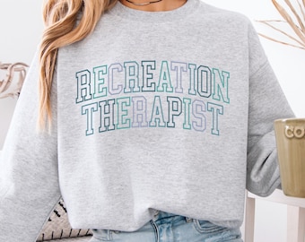 May include: A gray sweatshirt with the text "RECREATION THERAPIST" in a rainbow gradient.