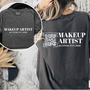 May include: A dark gray t-shirt with the text "MAKEUP ARTIST @CUSTOM.TEXT.HERE" on the front and a QR code with the text "SCAN ME" on the back.
