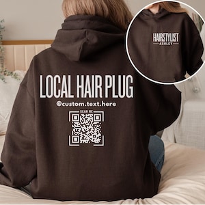 May include: A brown hoodie with a white graphic that says "LOCAL HAIR PLUG" and includes a QR code with the text "SCAN ME". The hoodie also has the text "HAIRSTYLIST ASHLEY" on the back.