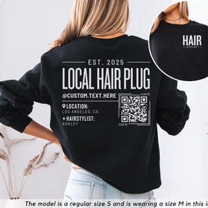 May include: Black sweatshirt with white text that reads "EST. 2025 LOCAL HAIR PLUG @CUSTOM.TEXT.HERE LOCATION: LOS ANGELES, CA + HAIRSTYLIST: ASHLEY" and a QR code. The text "SCAN ME" appears twice below the QR code.