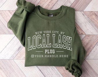 May include: Green sweatshirt with the text "NEW YORK CITY, NY LOCAL LASH PLUG @YOUR.HANDLE.HERE" printed in white.