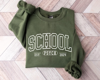 May include: A green sweatshirt with the text "SCHOOL PSYCH 2024" printed in white on the front.