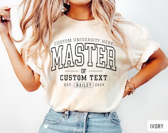 May include: A white t-shirt with the text "CUSTOM UNIVERSITY HERE MASTER OF CUSTOM TEXT EST. (HAILEY) 2024" printed in black. The model is wearing a size M.