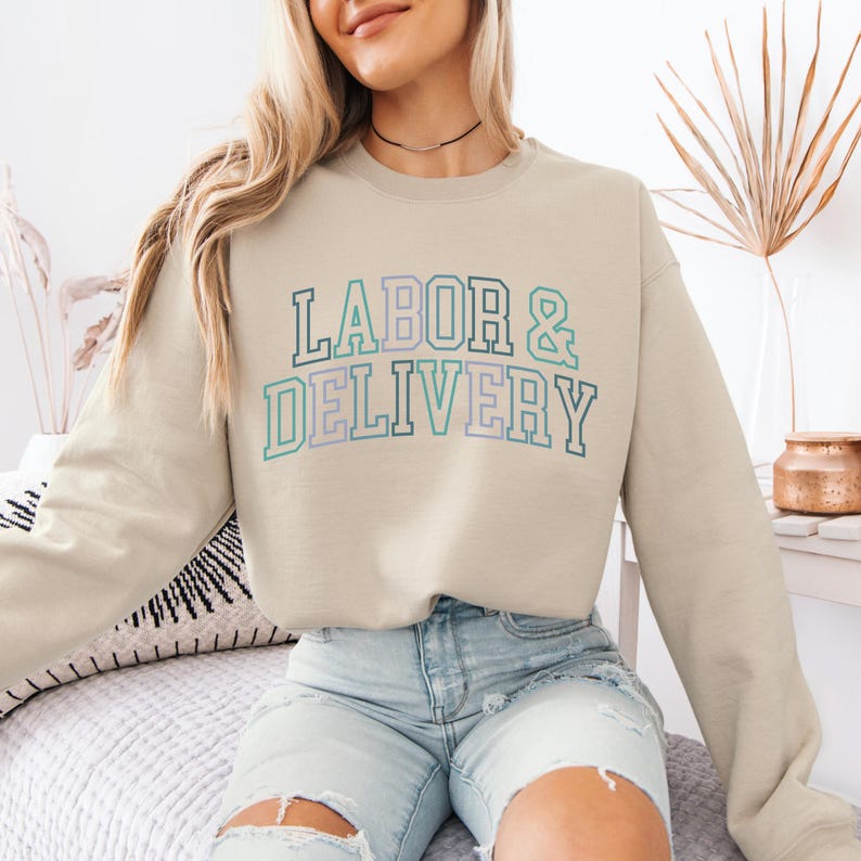 May include: A light beige sweatshirt with the text "LABOR & DELIVERY" in a colorful, varsity-style font.