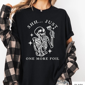 May include: Black t-shirt with a white skeleton holding a hair dye brush and the text "SHH... JUST ONE MORE FOIL".