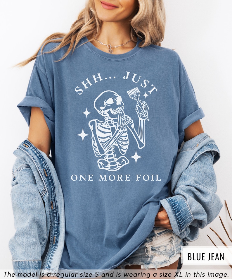 May include: A blue t-shirt featuring a white skeleton holding a hair dye brush with the text "SHH... JUST ONE MORE FOIL".
