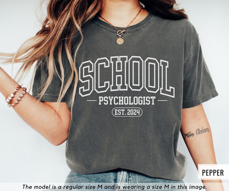 May include: A dark gray t-shirt with white text that reads "SCHOOL PSYCHOLOGIST EST. 2024".