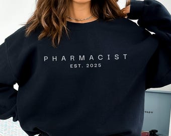 Könnte beinhalten: Schwarzer Pullover mit dem Text "PHARMACIST EST. 2025" in Weiß.