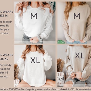 May include: Two models wearing white and beige sweatshirts with the size of the sweatshirt printed on the front. The model on the left is wearing a size M and the model on the right is wearing a size XL. The text below the models reads "The model is 5'10" (178cm) and regularly wears a size M for a relaxed fit / XL for an oversized fit."