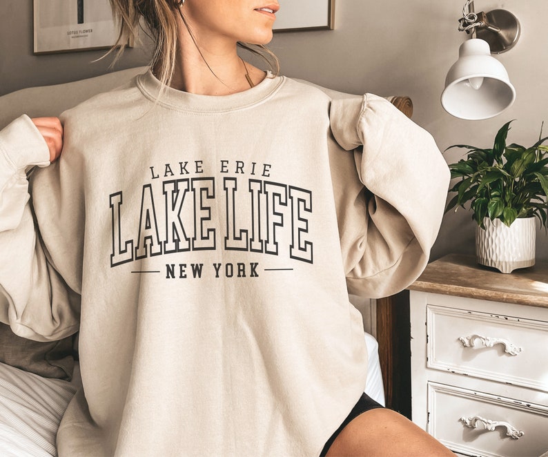 May include: A beige sweatshirt with black text that reads "LAKE ERIE LAKE LIFE NEW YORK".