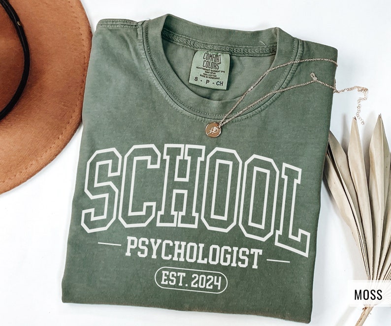 May include: A green t-shirt with white text that reads "SCHOOL PSYCHOLOGIST EST. 2024".