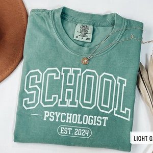May include: Light green t-shirt with the text "SCHOOL - PSYCHOLOGIST EST. 2024" printed in white.