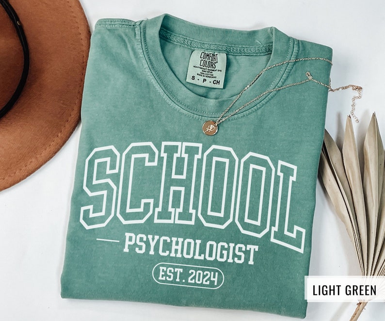 May include: Light green t-shirt with the text "SCHOOL - PSYCHOLOGIST EST. 2024" printed in white.