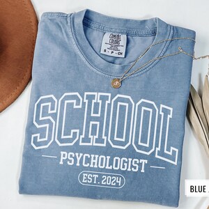 May include: A blue jean t-shirt with white text that reads "SCHOOL PSYCHOLOGIST EST. 2024".