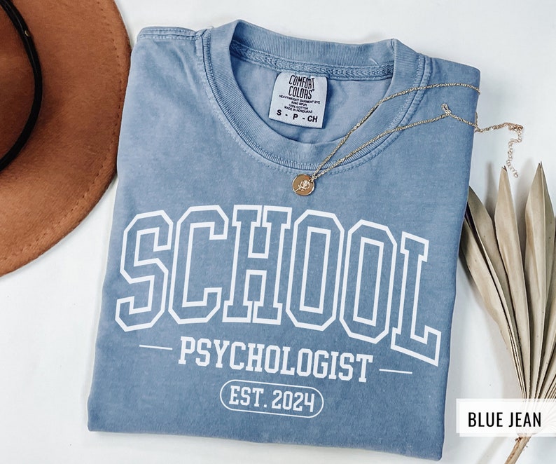 May include: A blue jean t-shirt with white text that reads "SCHOOL PSYCHOLOGIST EST. 2024".