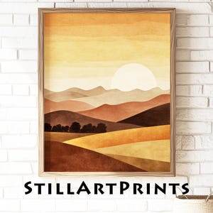 May include: A framed art print featuring a landscape scene with a warm color palette. The artwork depicts rolling hills, trees, and a large sun. The text "STILLARTPRINTS" is printed at the bottom of the frame.