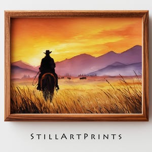 May include: Watercolor print of a cowboy on horseback silhouetted against a sunset. The artwork features a warm color palette of orange, yellow, and purple, with mountains in the background and tall grass in the foreground. The print is in a wooden frame. Text: STILLARTPRINTS.