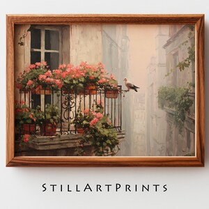May include: A framed print of a European street scene. A balcony with red flowers and a bird perched on the railing is in the foreground. The print has a warm color palette and the text "STILLARTPRINTS" at the bottom.
