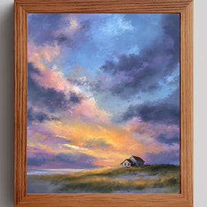 May include: A framed landscape painting depicts a coastal scene with a small white house under a dramatic sky. The sky is filled with vibrant colors of blue, purple, pink, and orange, suggesting a sunset or sunrise. The painting is in a wooden frame.