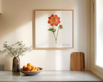 May include: A framed watercolor painting of a single orange dahlia flower with green leaves and a smaller orange flower bud. The painting is on a white background and has a light wood frame.
