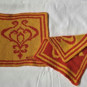 Könnte beinhalten: Zwei gehäkelte Topflappen in Gelb und Rot mit einem geometrischen Muster. Die Topflappen sind quadratisch und haben einen roten Rand.