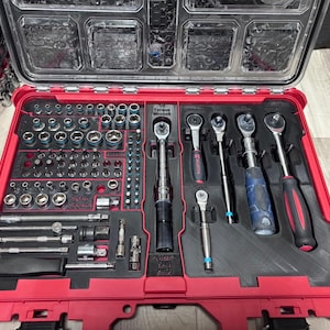Könnte beinhalten: Eine rote Werkzeugkiste mit transparentem Deckel, gefüllt mit einem umfassenden Satz an Werkzeugen. Die Werkzeuge umfassen Steckschlüssel, Ratschen und verschiedene Bits, die ordentlich in einer schwarzen Schaumstoffeinlage angeordnet sind. Die Werkzeugkiste ist geöffnet und zeigt die Werkzeugauswahl.
