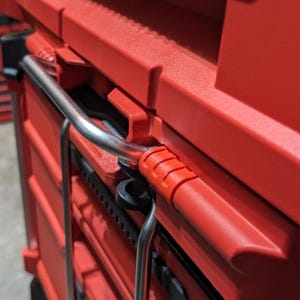 Pu&ograve; includere: Primo piano di un sistema di stoccaggio utensili rosso impilabile con maniglie nere e una maniglia in metallo. Il sistema &egrave; progettato per organizzare utensili e attrezzature. La maniglia &egrave; in metallo lucido.