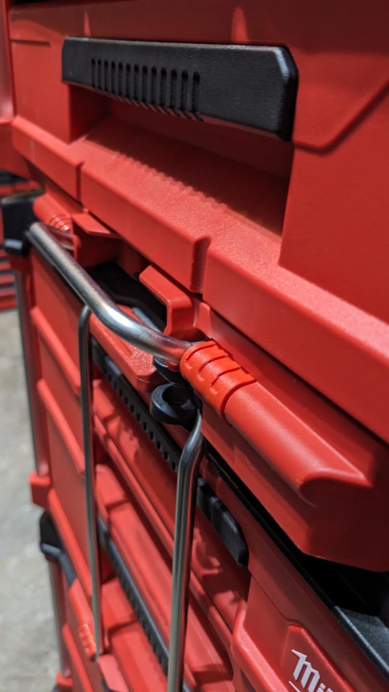 Pu&ograve; includere: Primo piano di un sistema di stoccaggio utensili rosso impilabile con maniglie nere e una maniglia in metallo. Il sistema &egrave; progettato per organizzare utensili e attrezzature. La maniglia &egrave; in metallo lucido.