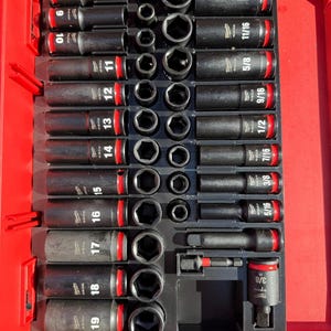 Könnte beinhalten: Ein Satz schwarzer Schlagschraubernüsse mit roten Akzenten, angeordnet in einem roten Kunststoffkoffer. Die Nüsse sind mit Größen in Zoll beschriftet, von 3/8 bis 3/4.