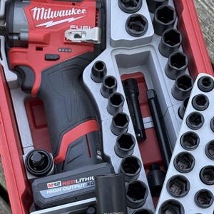 Könnte beinhalten: Ein rotes und schwarzes Milwaukee FUEL Schlagschrauber- und Steckschlüsselsatz. Das Set enthält eine Vielzahl schwarzer Steckschlüssel, Verlängerungen und einen Akku. Die Werkzeuge sind übersichtlich in einem roten Kunststoffkoffer angeordnet, ideal für Automobil- oder Bauprojekte.