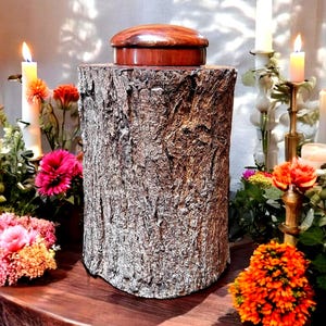 Peut inclure: Une urne en bois en forme de tronc d'arbre avec un couvercle brun foncé. L'urne est entourée de fleurs et de bougies.
