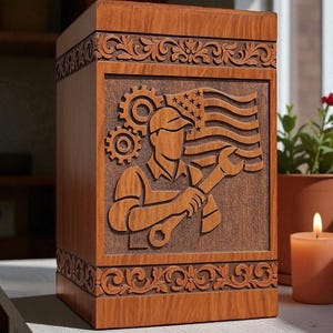 May include: Wooden urn with carved details. The front panel features a relief carving of a worker holding a wrench and the American flag, with gears in the background. The top and bottom edges have decorative floral patterns.